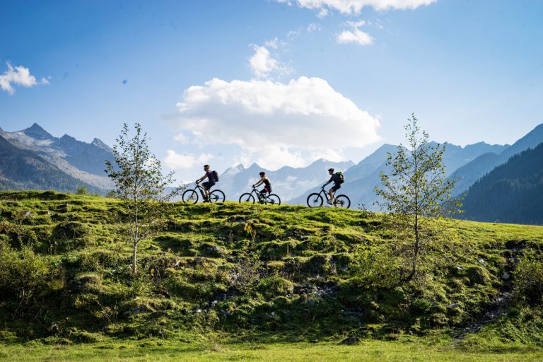 Zwei Radfahrer mit E-Mountainbikes auf Almwiese vor Bergpanorama in der Zillertalarena